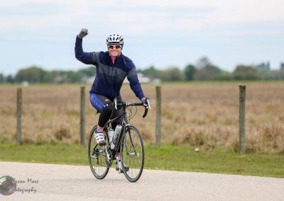 A man cycling on a rural road celebrating with a fist pump, promoting Bluebonnet Express bike rides.