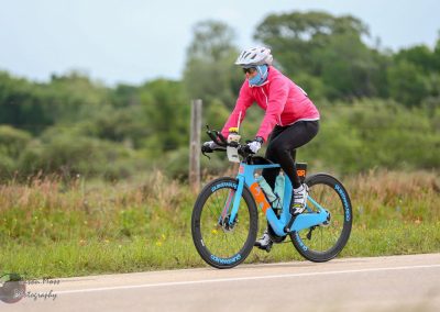 Bright blue electric bike on scenic rural road with cyclist wearing pink jacket and helmet.