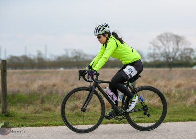 High-performance cyclist riding a black bike in a rural outdoor setting, wearing bright green athletic gear and safety helmet.