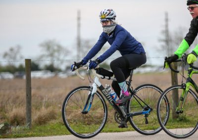 1. Female cyclist riding a BMC road bike on a cloudy day in outdoor setting.