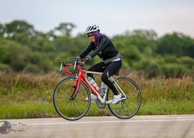 Bright woman cyclist wearing helmet and sunglasses riding a road bike in open countryside.