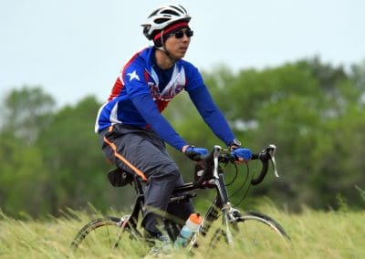 Vibrant cyclist riding mountain bike outdoors in scenic green landscape, representing Bluebonnet Express cycling team.