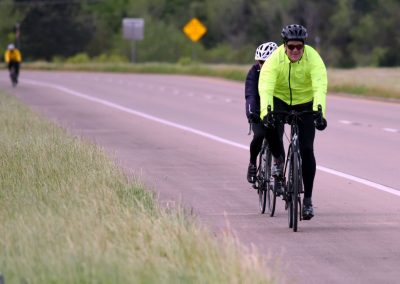 Bright yellow cycling jacket on a rider on a scenic bike path with others in the background.
