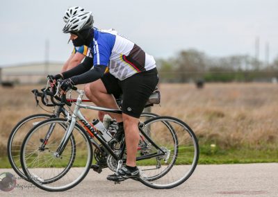 High-performance cyclist wearing blue and black cycling gear riding on a road in a rural area.