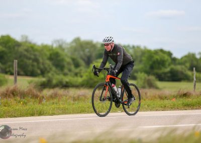 Vibrant cyclist riding on scenic rural road with lush greenery background.