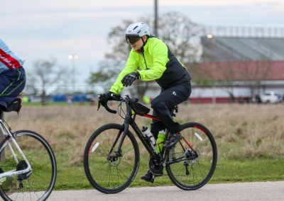 Colorful cyclist wearing bright yellow and black riding a bike outdoors, promoting Bluebonnet Express service.