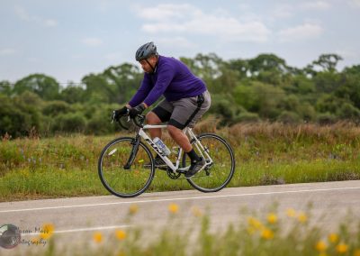 Vegan cyclist riding on scenic Texas highway with wildflowers and green trees in the background.