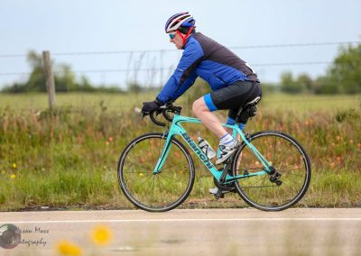 Bright blue Bianchi road bike with rider in cycling gear on a scenic countryside trail.