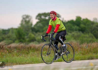 Bright green and red cyclist riding on the Bluebonnet Express trail surrounded by nature.