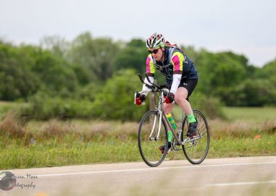 Vibrant cyclist racing outdoors on a scenic trail with lush green trees in the background.