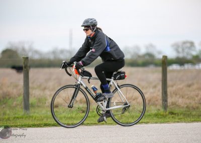 Mid-distance cyclist riding a bike on a rural path with a cloudy sky.