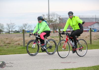 Bright neon cycling jackets worn by two female cyclists riding bikes outdoors on a cloudy day.