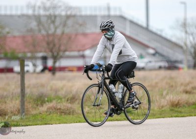 Bright-eyed cyclist wearing a helmet and mask riding a black Trek road bike along a scenic trail.
