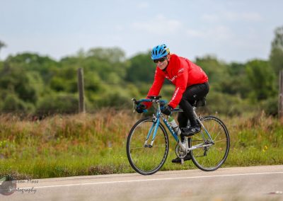 Bright blue bike with a smiling cyclist wearing a red jacket and helmet riding through scenic countryside.