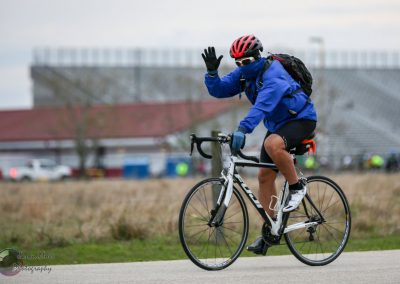 Bright blue cyclist wearing helmet, mask, and gloves riding a bike during Bluebonnet Express event.