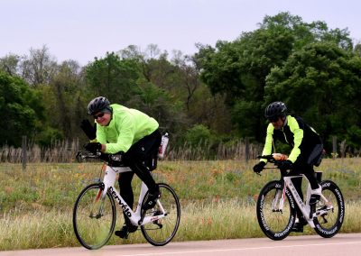 Bright yellow cycling jackets on two bikers riding on a scenic rural road during daytime.