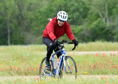 Vibrant cyclist riding through a scenic trail with wildflowers in a lush green landscape.