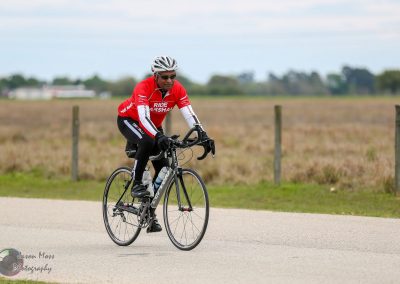 Man riding a bicycle on rural road with open fields, promoting Bluebonnet Express cycling service.
