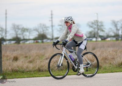 Comfortable woman riding a scenic bike trail in the countryside, promoting Bluebonnet Express cycling event.