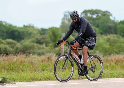 Helmeted cyclist riding a bike with orange handlebars on a rural road during daytime.
