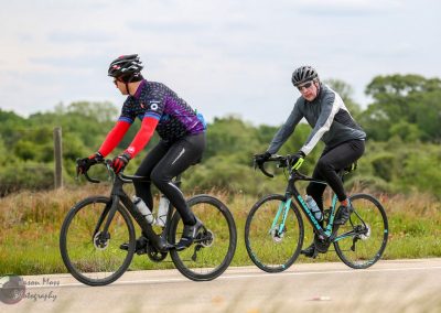 Energetic cyclists riding along a scenic countryside road on a sunny day.