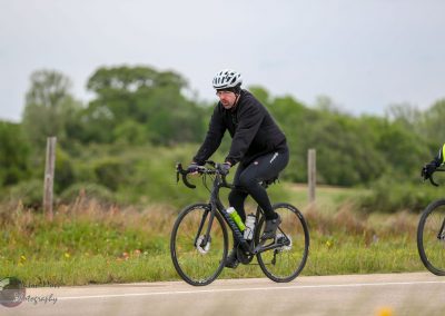 Men riding Bluebonnet Express bicycle on scenic rural trail, green landscape background, eco-friendly cycling lifestyle.