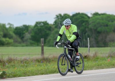 Bright yellow cycling jacket on male cyclist riding on scenic rural road during daytime.