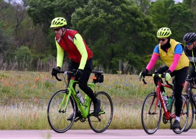 Bright cycling enthusiasts riding on a scenic trail with vibrant wildflowers and lush green trees in the background.
