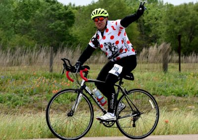 Bright cyclist in polka dot jersey riding on scenic trail with colorful wildflowers and green trees.
