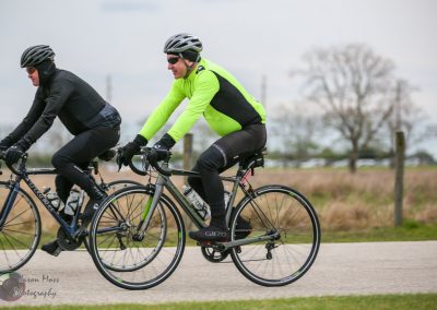 Cyclists riding bikes outdoors on a rural road, promoting Bluebonnet Express cycling event.