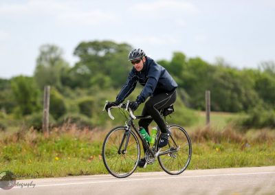 Cyclist riding a road bike in green outdoor landscape, promoting Bluebonnet Express bike service.