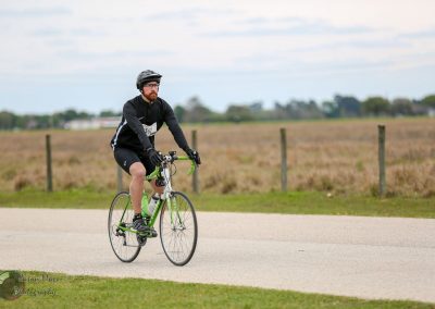 Cyclist riding a green bike on a rural road during daytime.