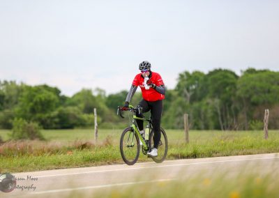 Vegan cyclist riding a bike on a country road, drinking water during a fitness ride, outdoor cycling event, Bluebonnet Express.