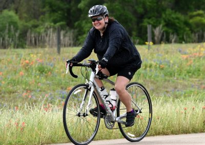 Vibrant woman cycling on a scenic trail with a field of wildflowers, showcasing Bluebonnet Express bike.