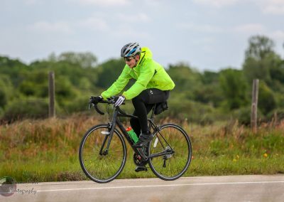 Bright green jacket cyclist riding a road bike outdoors during daytime.
