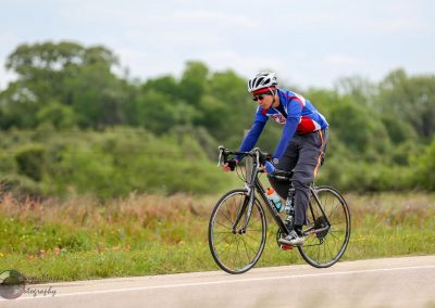 Bright blue and red cycling jersey, male cyclist riding a road bike outdoors on a scenic trail.
