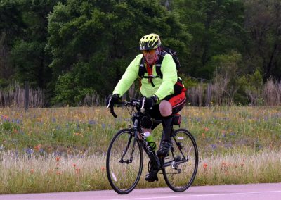 Vibrant cyclist riding through a scenic wildflower meadow on Bluebonnet Express route.