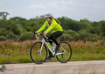 Vibrant cyclist riding a bike along scenic trail in nature, promoting Bluebonnet Express outdoor biking adventures.