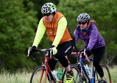 Brightly colored cycling apparel on two riders enjoying outdoor bike ride on trail amid lush green landscape.