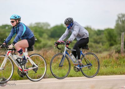 Brightly dressed cyclists riding on a scenic outdoor trail, promoting Bluebonnet Express bike tours.