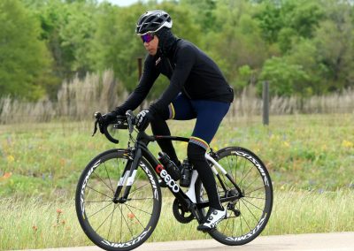 Velo cyclist riding on a trail with greenery during daytime, promoting Bluebonnet Express bike services.