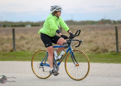 Bright green jacket cyclist riding a Cannondale road bike on a paved trail in open countryside.
