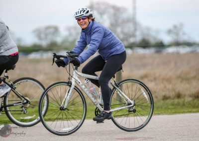 Bright woman smiling while riding a bike on a scenic trail, promoting Bluebonnet Express cycling tours.