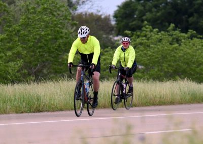 Bright yellow cycling jackets on two bikers riding along scenic countryside road.