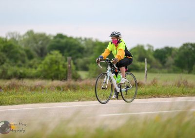 Bright yellow safety jacket cyclist riding on rural road during daytime.
