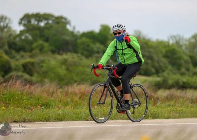 Bright green cyclist with blue mask riding on scenic rural road for Bluebonnet Express event.