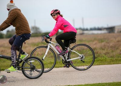 Bright pink cycling jacket and helmet, female rider on a white bike on a scenic trail.