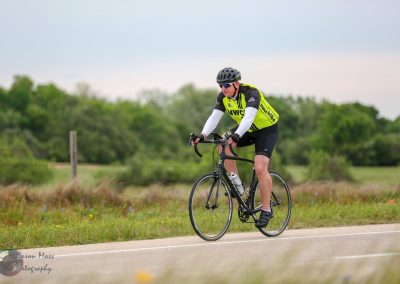 Cyclist riding a bike through scenic open landscape with greenery and overcast sky.