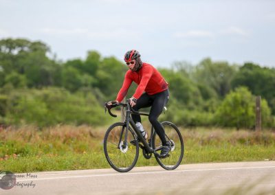 Endurance cyclist riding a black road bike through scenic rural landscape during daytime.