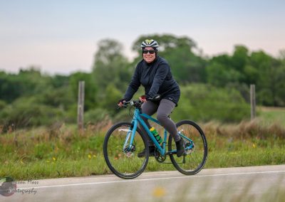 Vibrant woman riding a blue bike outdoors during daytime, promoting healthy lifestyle and cycling fun.